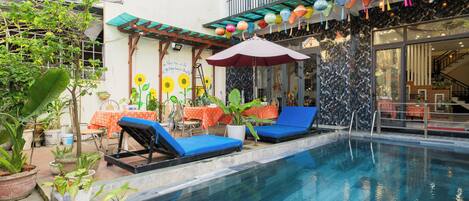 A pool area with lounge chairs, a table with an orange tablecloth, and potted plants.