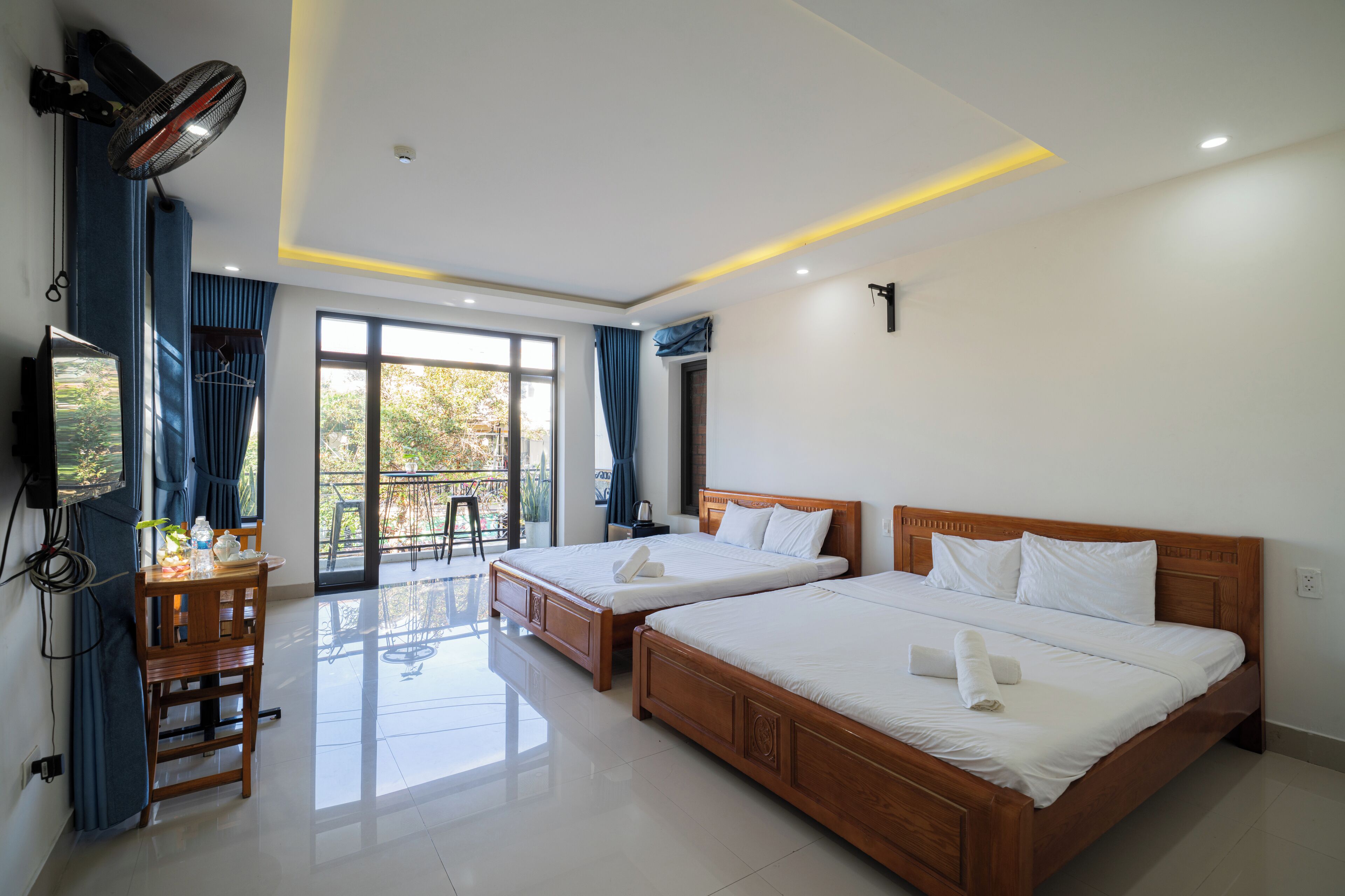 Habitación de hotel con dos camas, televisión, balcón y zona de comedor.