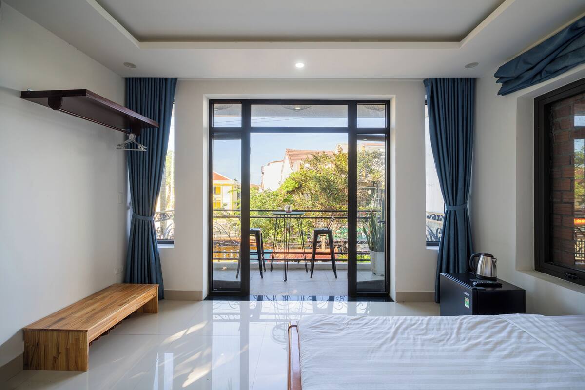 A bedroom with a bed, a bench, a table with chairs, and a balcony with a view.