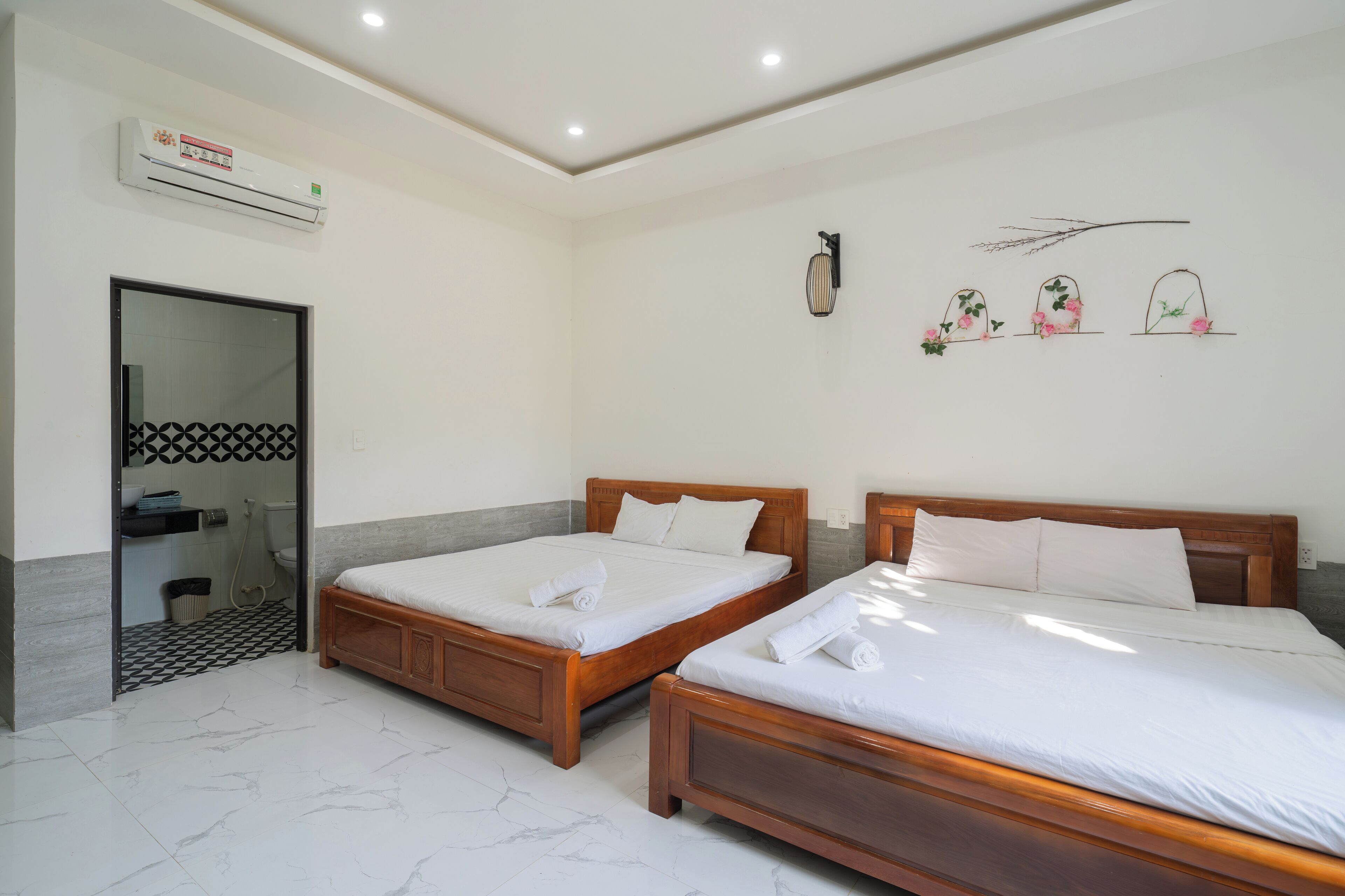 Una habitación de hotel con dos camas de madera, un baño con piso estampado y un aire acondicionado instalado en la pared.