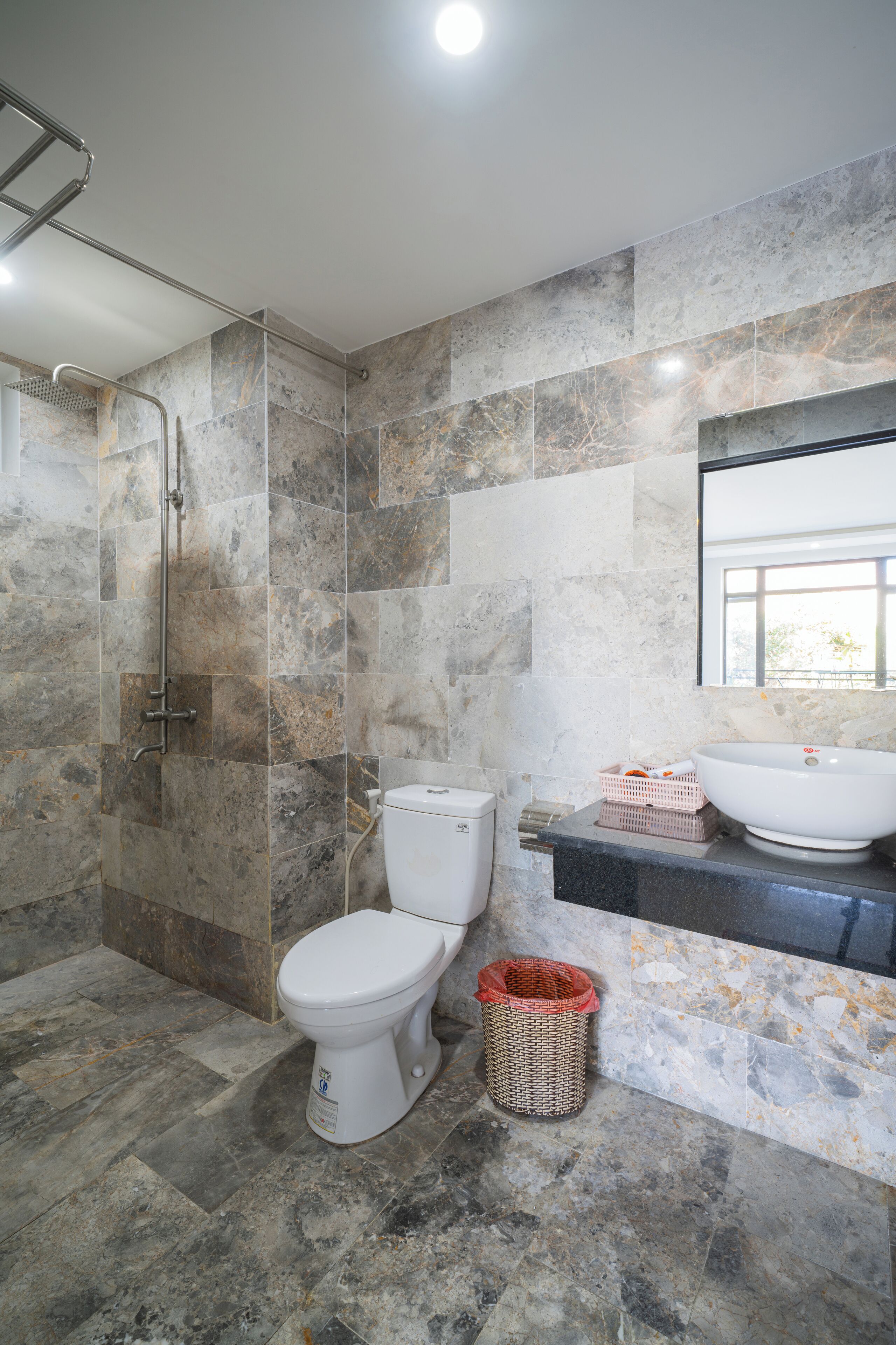 A bathroom with a shower, toilet, sink, and marble walls.