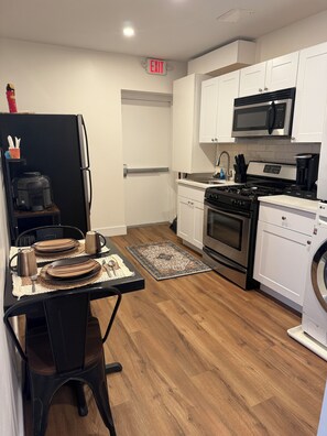 A modern kitchen with a dining area, featuring a refrigerator, microwave, stove, and washing machine. - Monthly stay near Light Rail + NYC rooftop views (Jersey City)