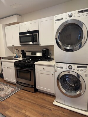 A compact kitchen with white cabinets, a microwave, a stove, and a stacked washer and dryer. - Monthly stay near Light Rail + NYC rooftop views (Jersey City)