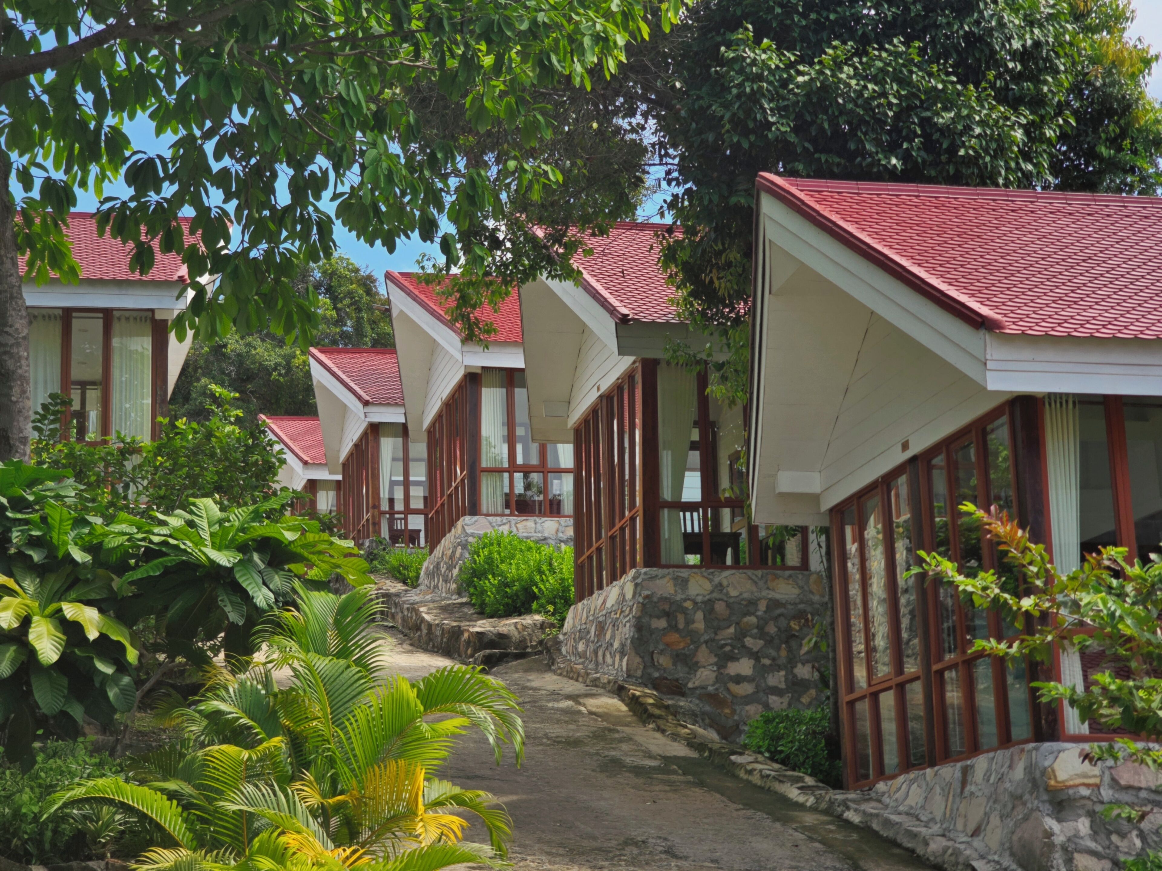A row of bungalow-style buildings with red roofs, stone walls, and large windows. - Alicia resort (Koh Rong)