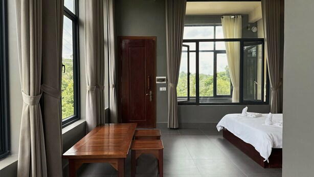 A room with a bed, a wooden table, a bench, a wardrobe, and large windows with curtains. - Alicia resort (Koh Rong)
