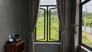 A room with a large window, curtains, a wooden shelf with items, and a stand. - Alicia resort (Koh Rong)
