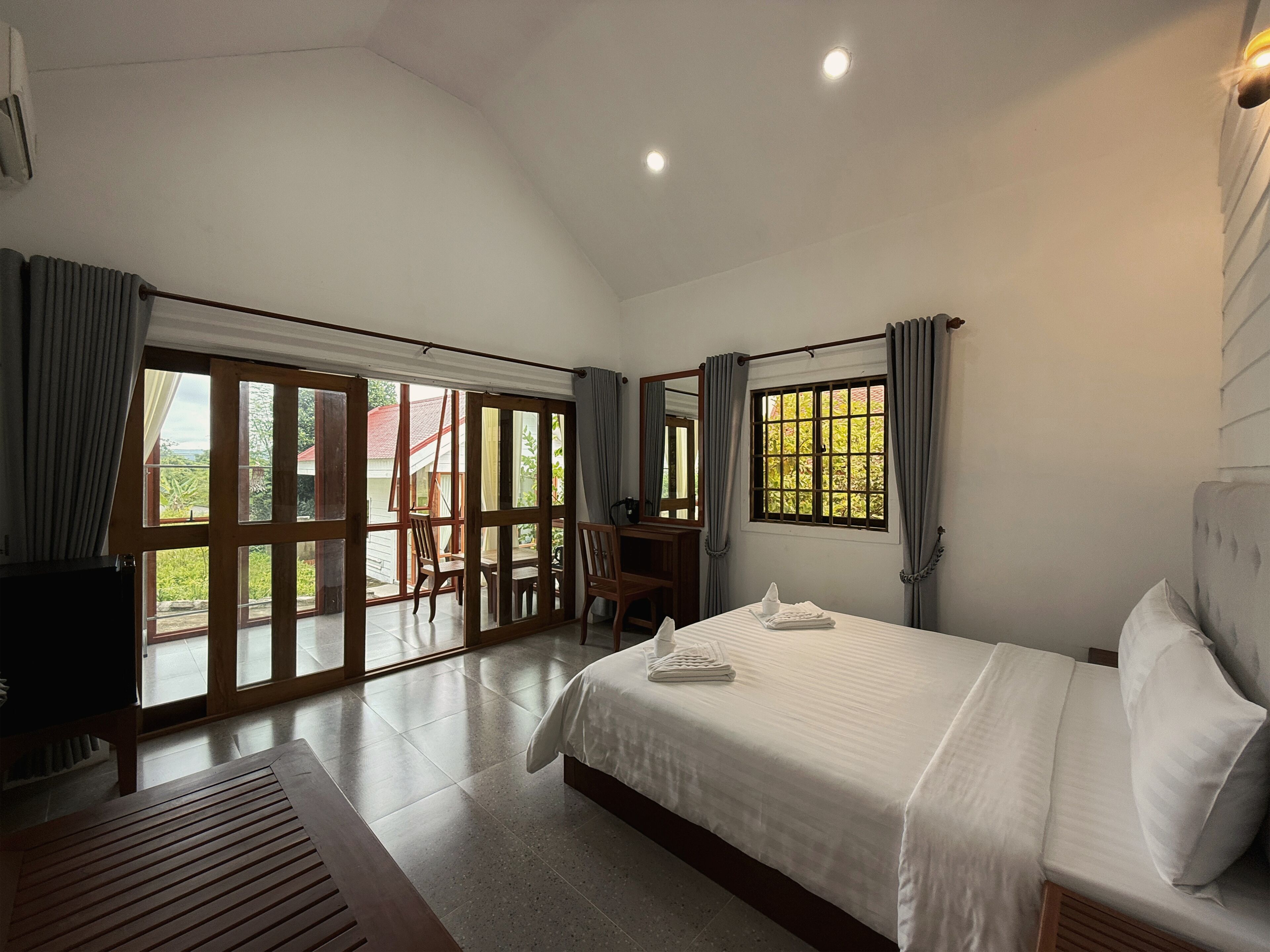 A bedroom with a bed, a desk, a chair, and a large sliding glass door leading to an outdoor area.