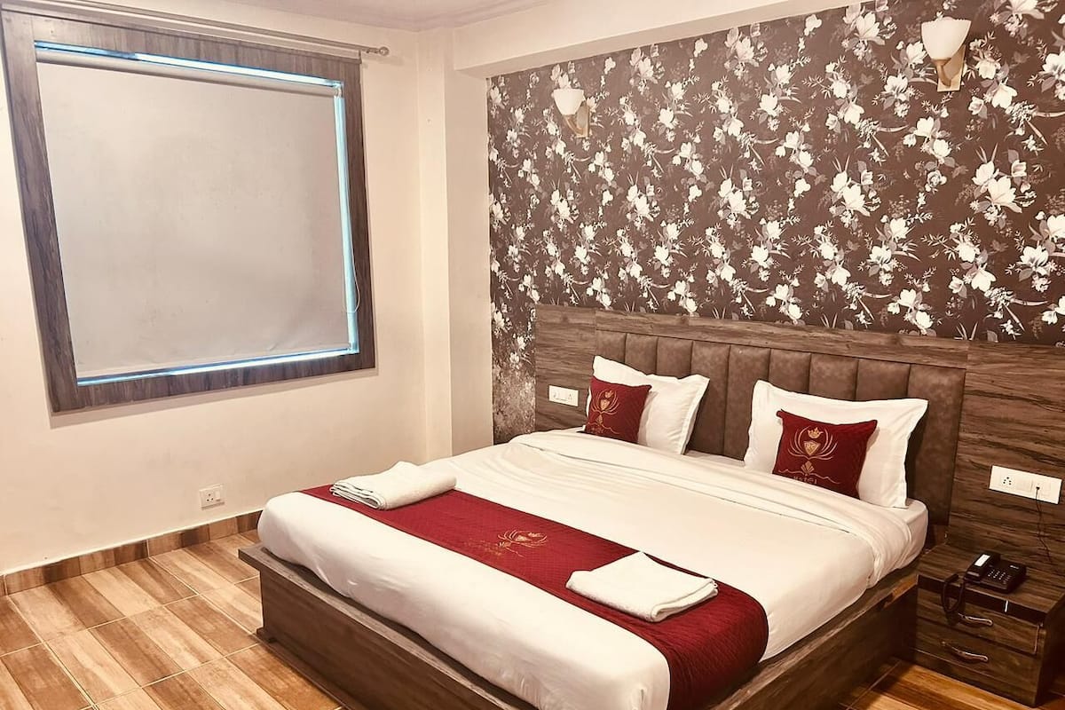 Habitación de hotel con una cama grande, cabecera de madera, papel tapiz floral y una ventana con vistas.