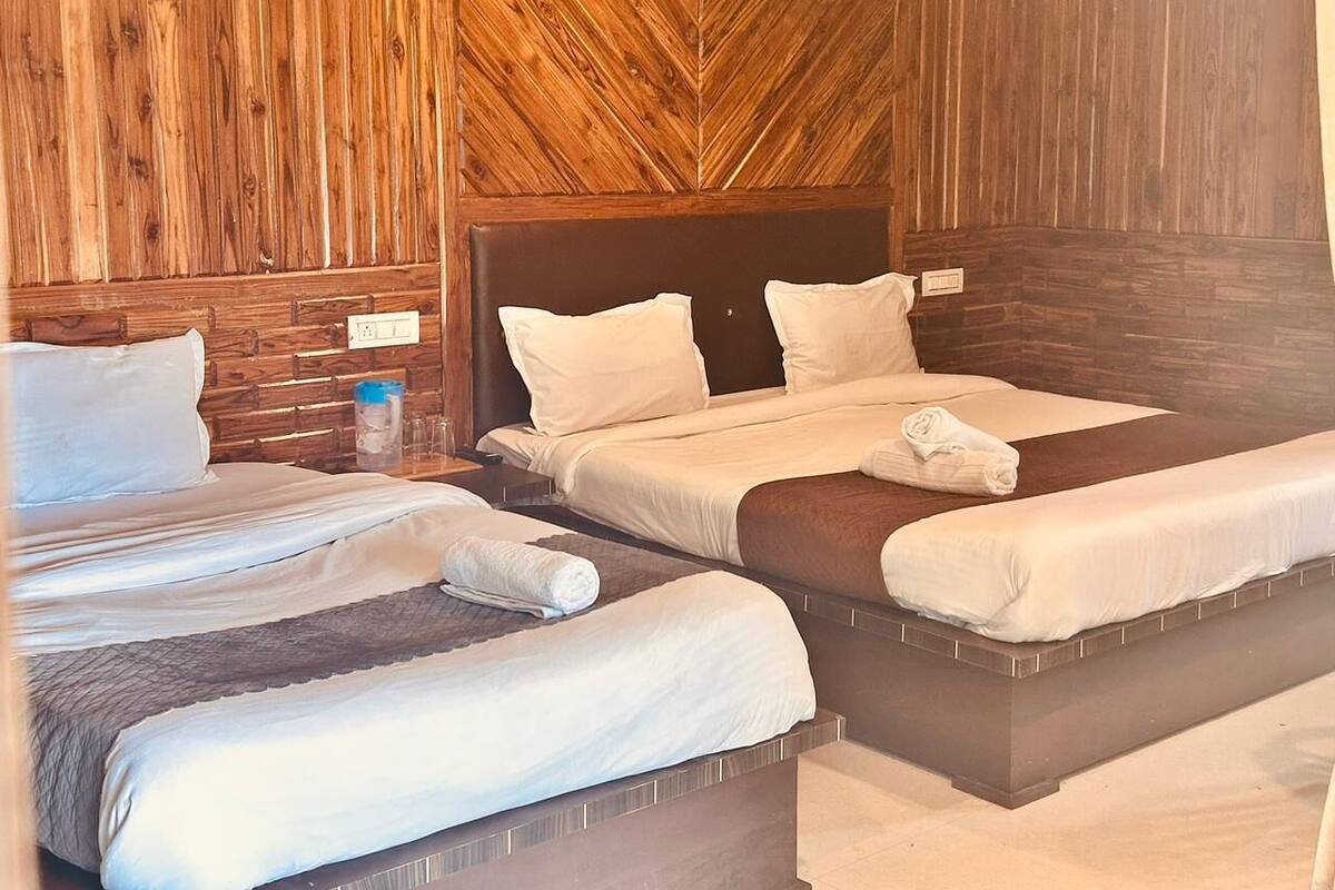 Habitación de hotel con tres camas, paredes de paneles de madera y un cabecero moderno.