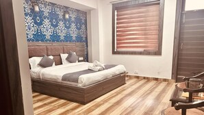 Ένα υπνοδωμάτιο με ένα κρεβάτι, ένα ξύλινο πάτωμα, έναν τοίχο με ένα μπλε σχέδιο, ένα παράθυρο με περσίδες και μια πόρτα.