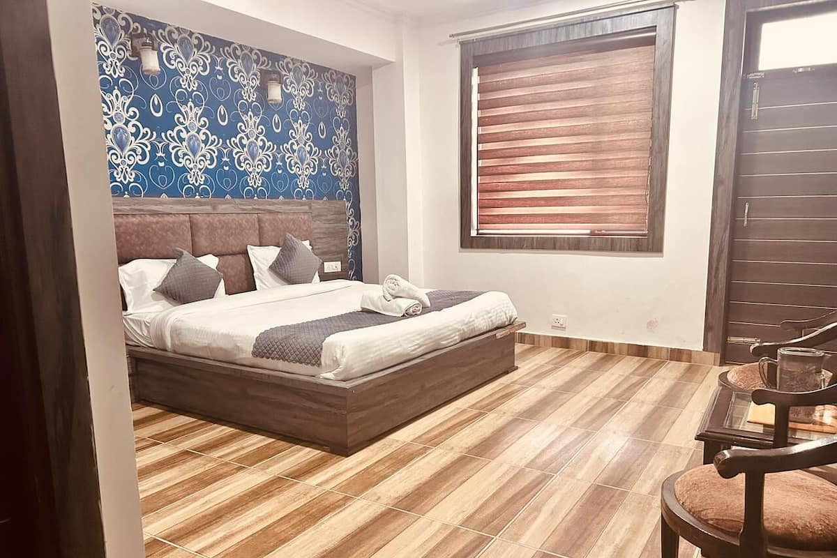 Un dormitorio con cama, suelo de madera, pared con diseño azul, ventana con persianas y puerta.