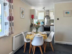 Un coin repas avec une table dressée pour quatre personnes, une cuisine en arrière-plan et un radiateur au mur.