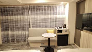 Une chambre d’hôtel avec un canapé, une petite table ronde, une table de chevet avec une bouilloire et un téléviseur.