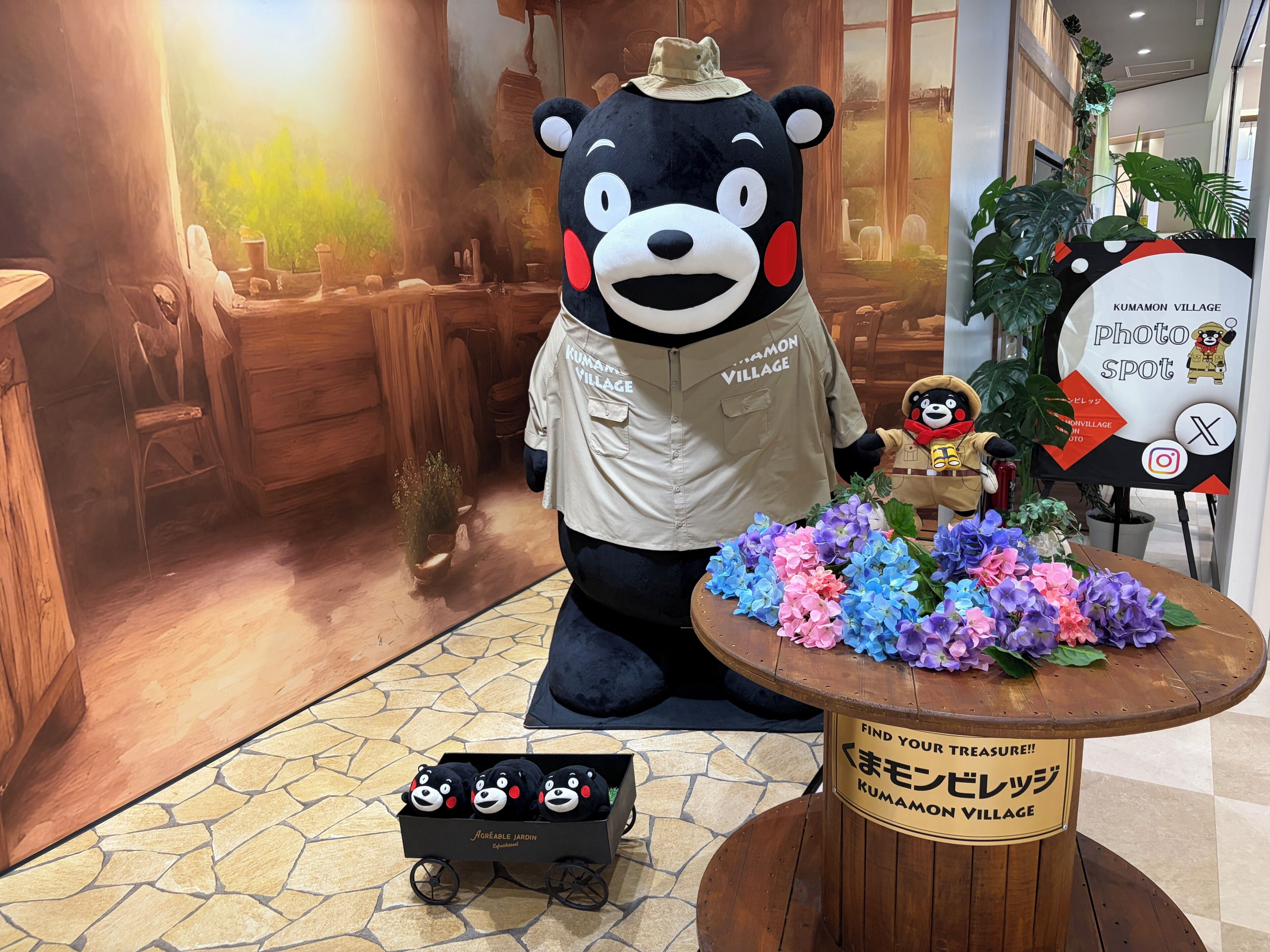 Una mascota d'ós en un comerç amb mobiliari de fusta i un cartell que diu 'Kumamon Village'.