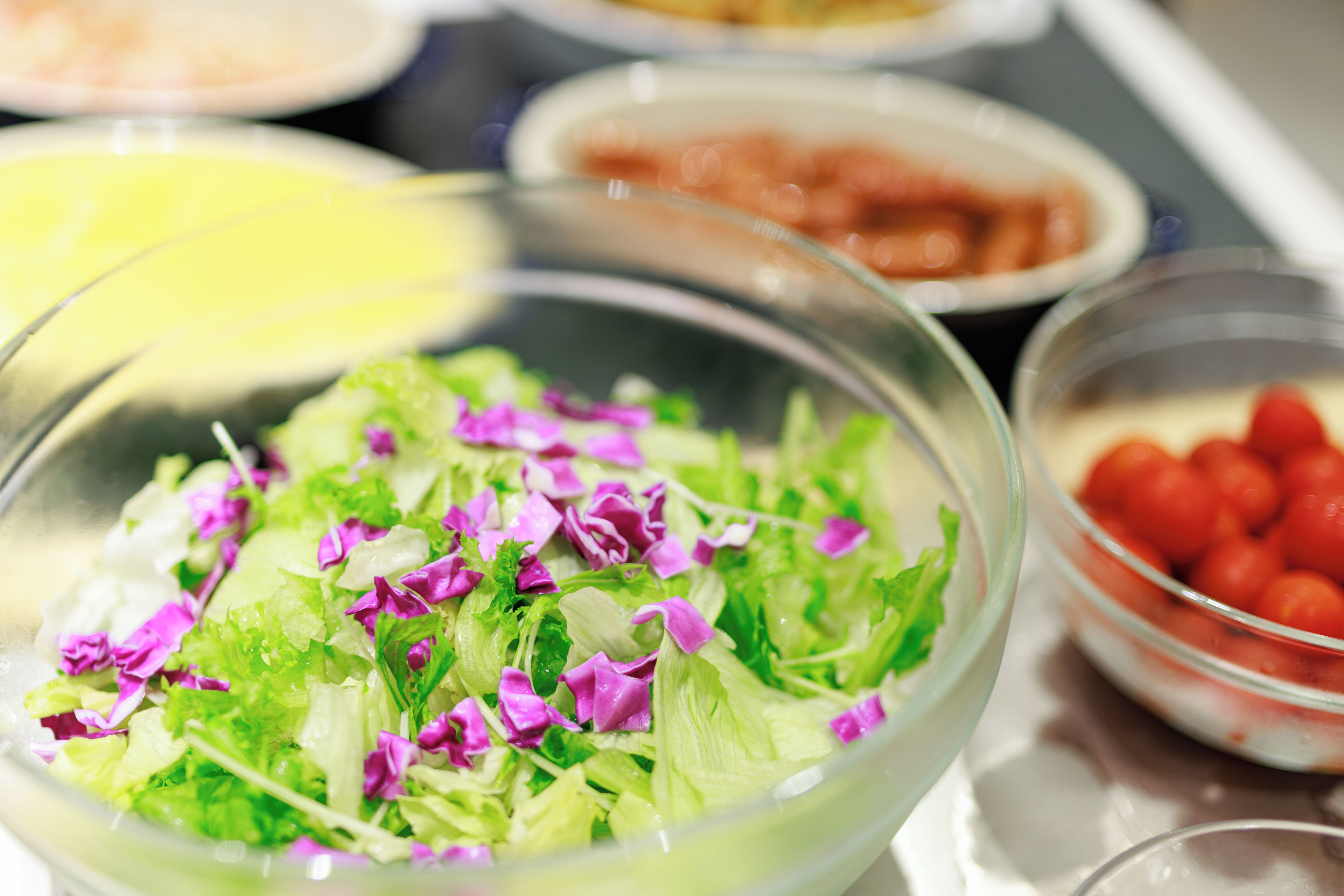 Un tazón de ensalada con diferentes verduras de hoja y flores moradas.