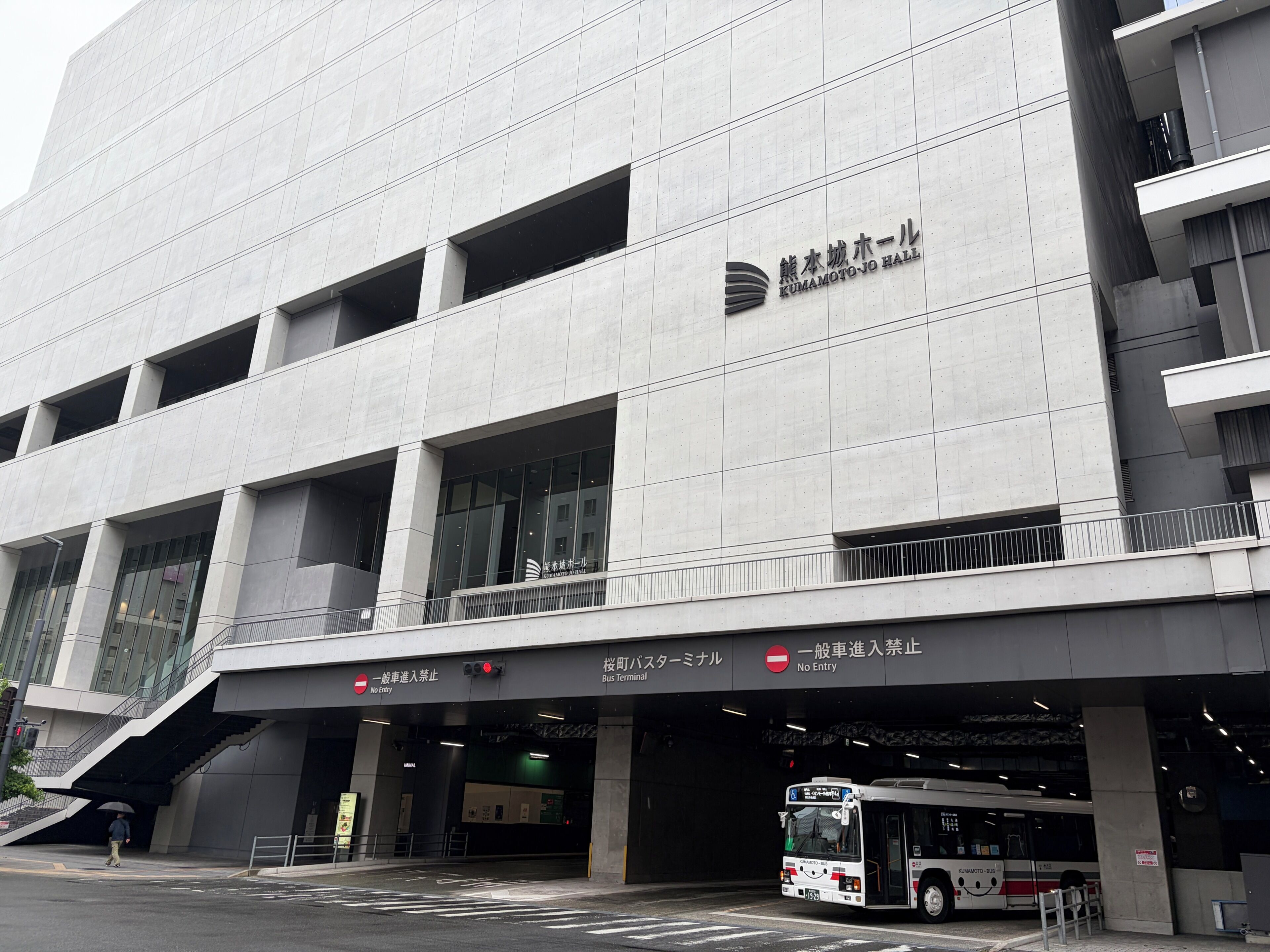 Un bâtiment moderne doté d’une grande entrée, d’un panneau indiquant l’emplacement du terminus de bus et d’un autobus garé à l’extérieur.
