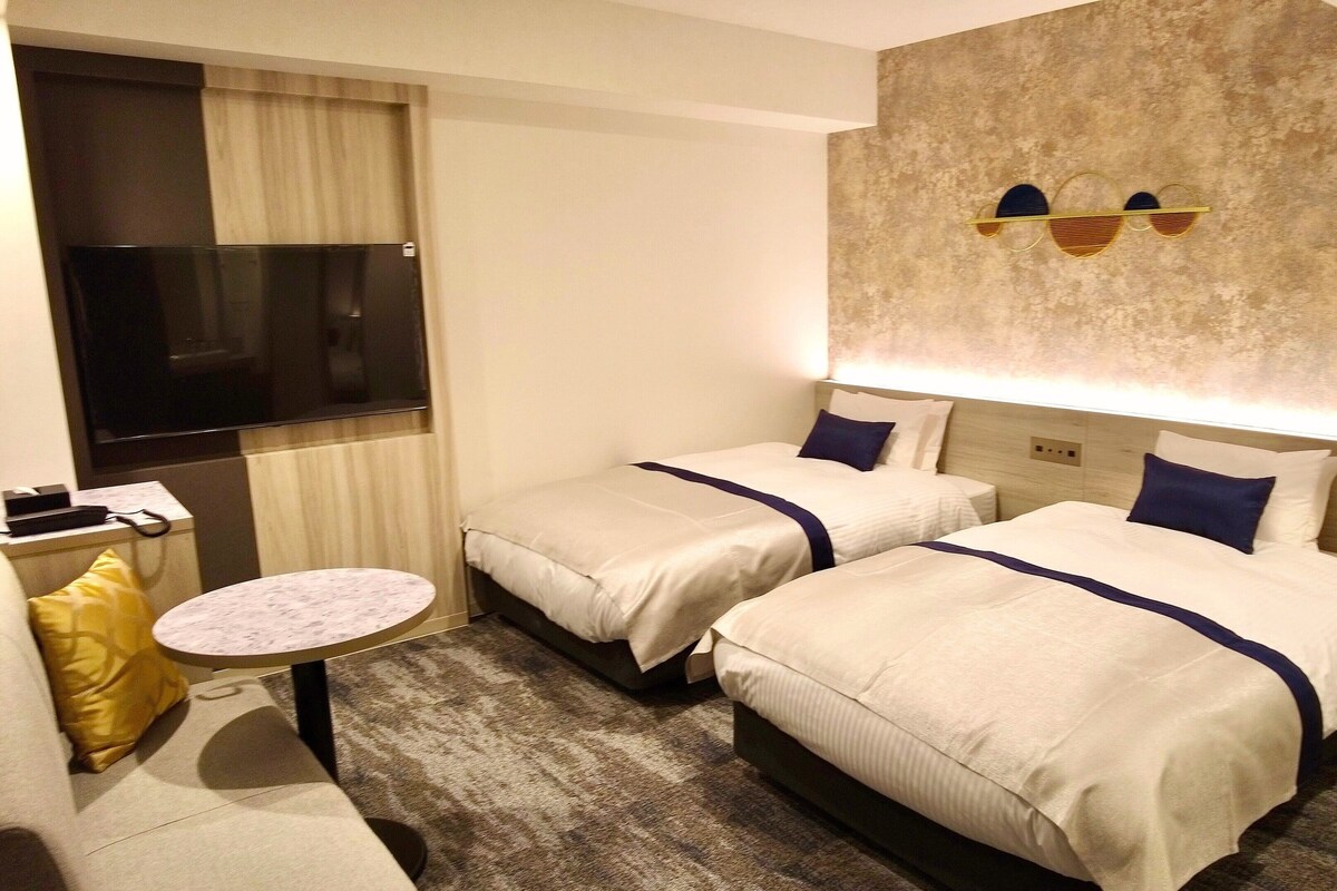A hotel room with two beds, a small round table, a TV, and a wall-mounted light fixture.