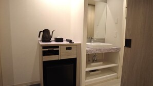 A compact hotel bathroom with a sink, mirror, and a small cabinet with a kettle and phone. - HOTEL AMANEK Kumamoto (Kumamoto)