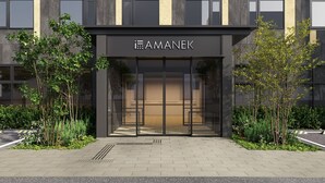 A modern building entrance with a glass facade, a sign reading 'AMANEK,' and a paved walkway with greenery. - HOTEL AMANEK Kumamoto (Kumamoto)