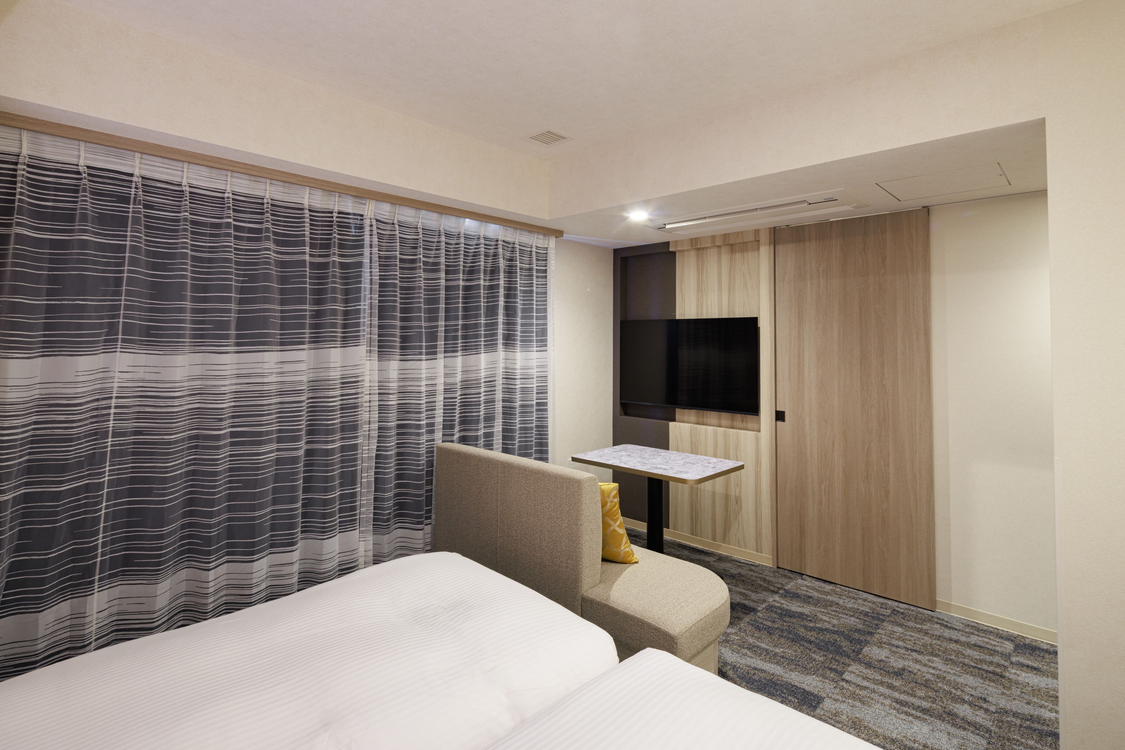 Ein Hotelzimmer mit einem Bett, einem Sessel, einem kleinen Tisch, einem Fernseher und einem Kleiderschrank.