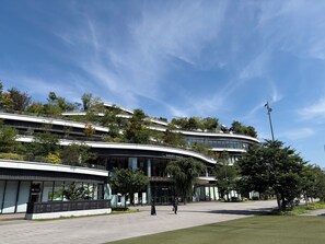 A modern building with a curved facade, a sign for 'SAKURA MACHIK,' and a pedestrian walkway. - HOTEL AMANEK Kumamoto (Kumamoto)