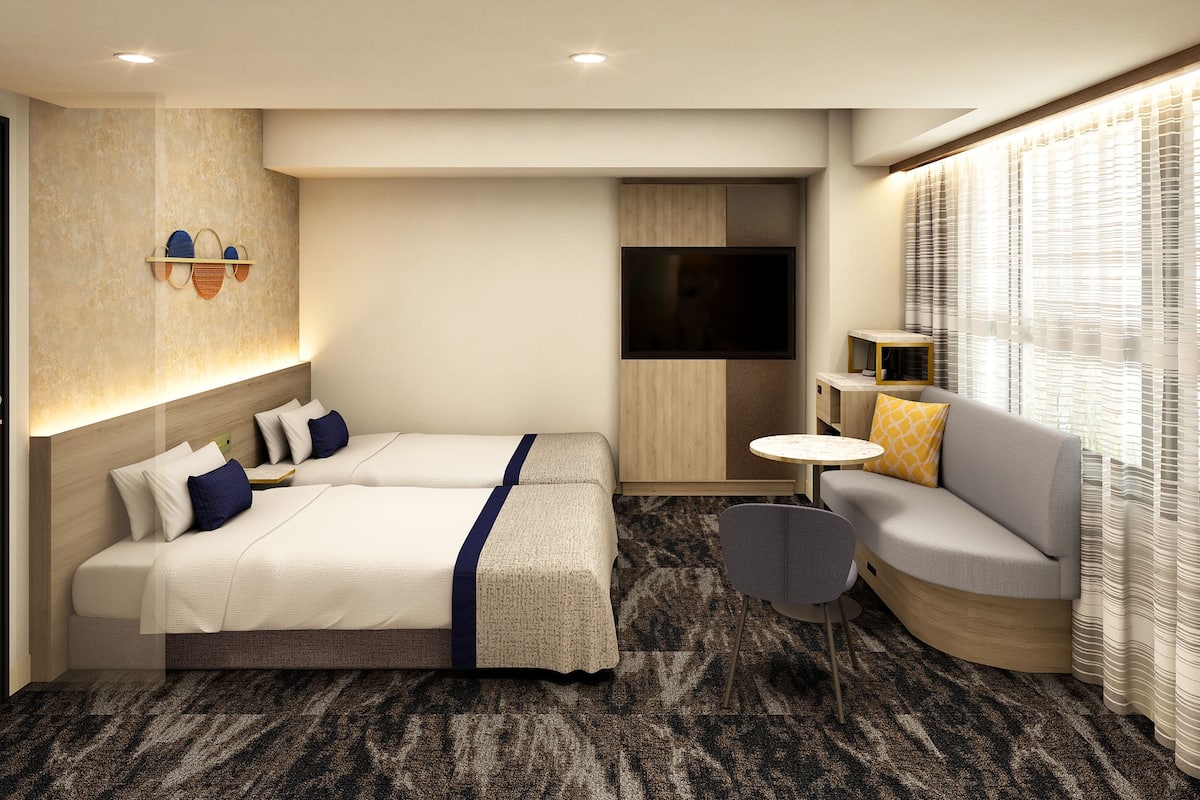A hotel room with two beds, a sofa, a small table, and a TV.