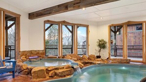 Een wellnessruimte met een jacuzzi, grote ramen, houten balken en een stenen muur.