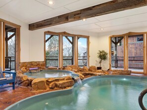 Ein Wellnessbereich mit Whirlpool, großen Fenstern, Holzbalken und einer Steinwand.