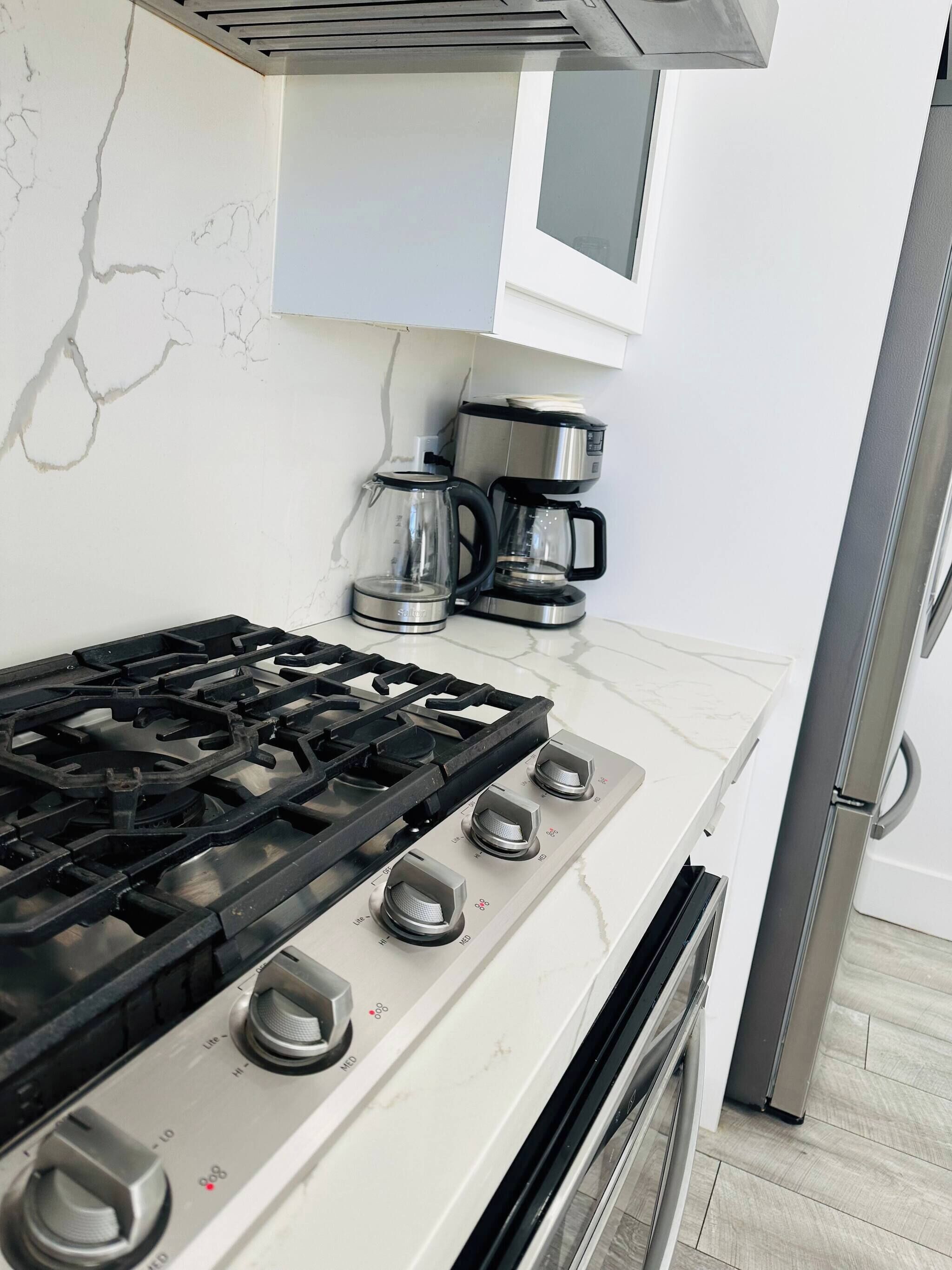 A kitchen with a gas stove, coffee maker, and a refrigerator.