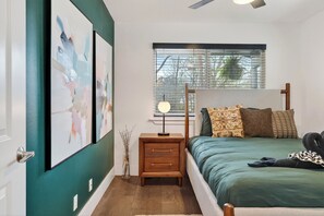 A bedroom with a bed, a nightstand, a lamp, a window with blinds, and artwork on the wall. - Stylish East Austin Home + Patio Dining + Minutes to Downtown | Eastside Keys (Austin)