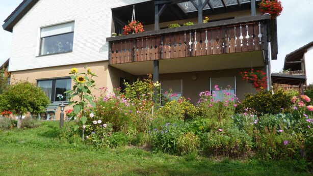 A two-story house with a balcony, surrounded by a garden with various flowers and plants. - Holiday Apartment for 2 People (35 m²) in Weilheim (Baden-Württemberg) (Weilheim)