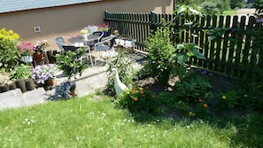 Een tuin met een tafel en stoelen, een witte beeldhouwkunst van een vogel, en een houten omheining.