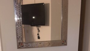 Casa de banho com espelho, televisão e prateleira de metal com duas tigelas.