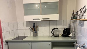 Uma cozinha compacta com armários brancos, uma pia de aço inoxidável, uma chaleira e uma cafeteira.
