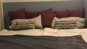 Uma cama com almofadas vermelhas e estampadas, uma cabeceira escura e um quadro fixado na parede.