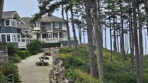 A coastal property with a gravel pathway leading to a wooden deck, surrounded by dense forest and overlooking the sea.