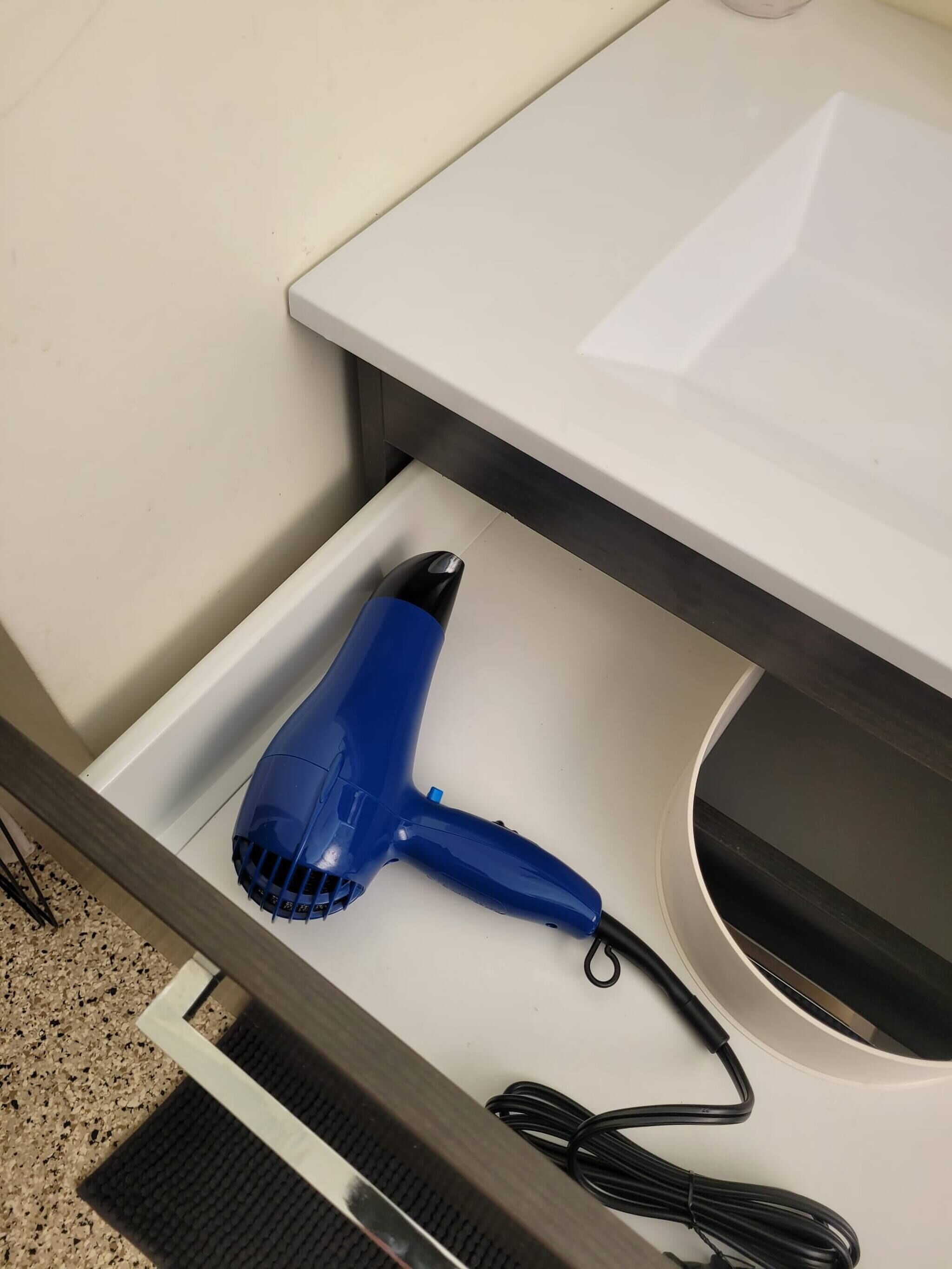 Ein blauer Haartrockner in einer Schublade mit einer weißen Arbeitsplatte und einem schwarzen Kabel.