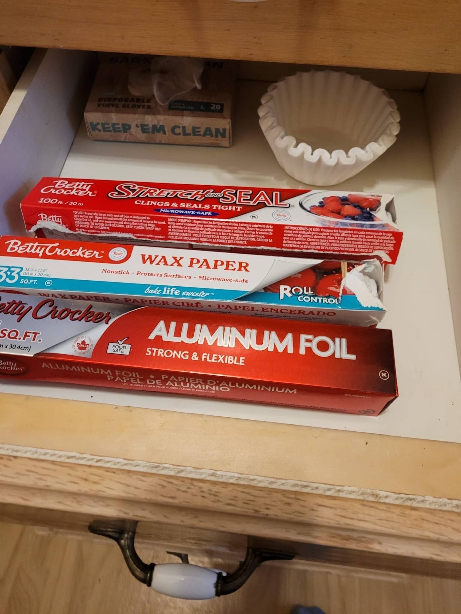 Un cajón con diversos utensilios de cocina, incluyendo papel encerado Betty Crocker, papel de aluminio y una caja de cinta adhesiva para la cocina.