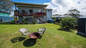 Une maison à deux étages dotée d’un balcon, d’un espace extérieur aménagé et couvert, et d’un grand récipient en métal.