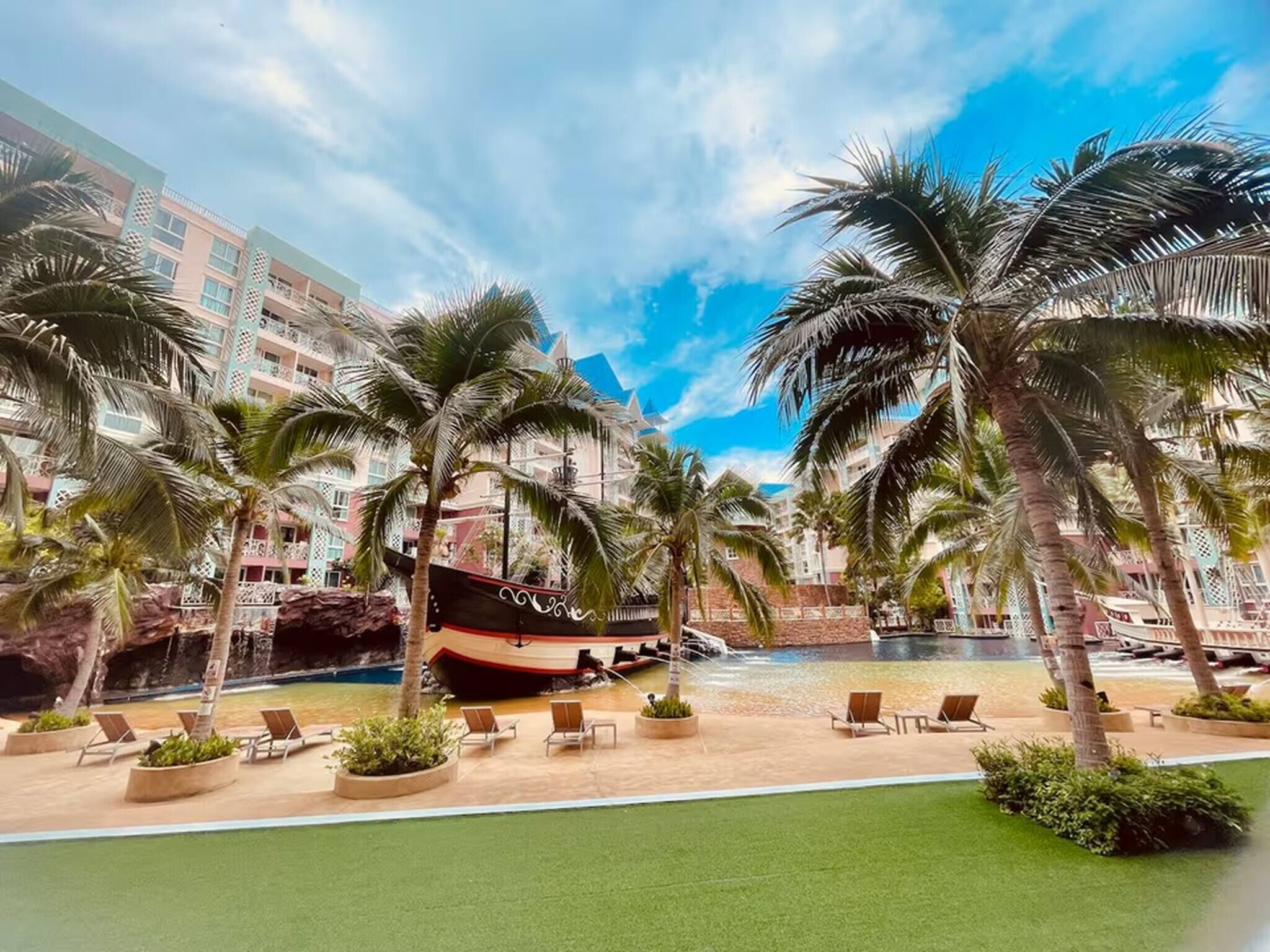 Un resort con piscina, palmeras y un barco.