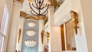 Een ruime lobby met een kroonluchter, zitgedeeltes en decoratieve wandpanelen.