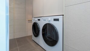 A modern laundry room with two front-loading washing machines, a tiled floor, and a plain wall. - KIMSTEL Jongno (Seoul)