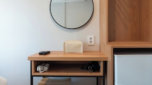 A room with a round mirror, a small table with a remote control, a tissue box, and a shelf with a camera and cables. - KIMSTEL Jongno (Seoul)