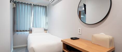 Une chambre d’hôtel comprenant un lit, un bureau avec une chaise, un miroir rond et un appareil de climatisation.