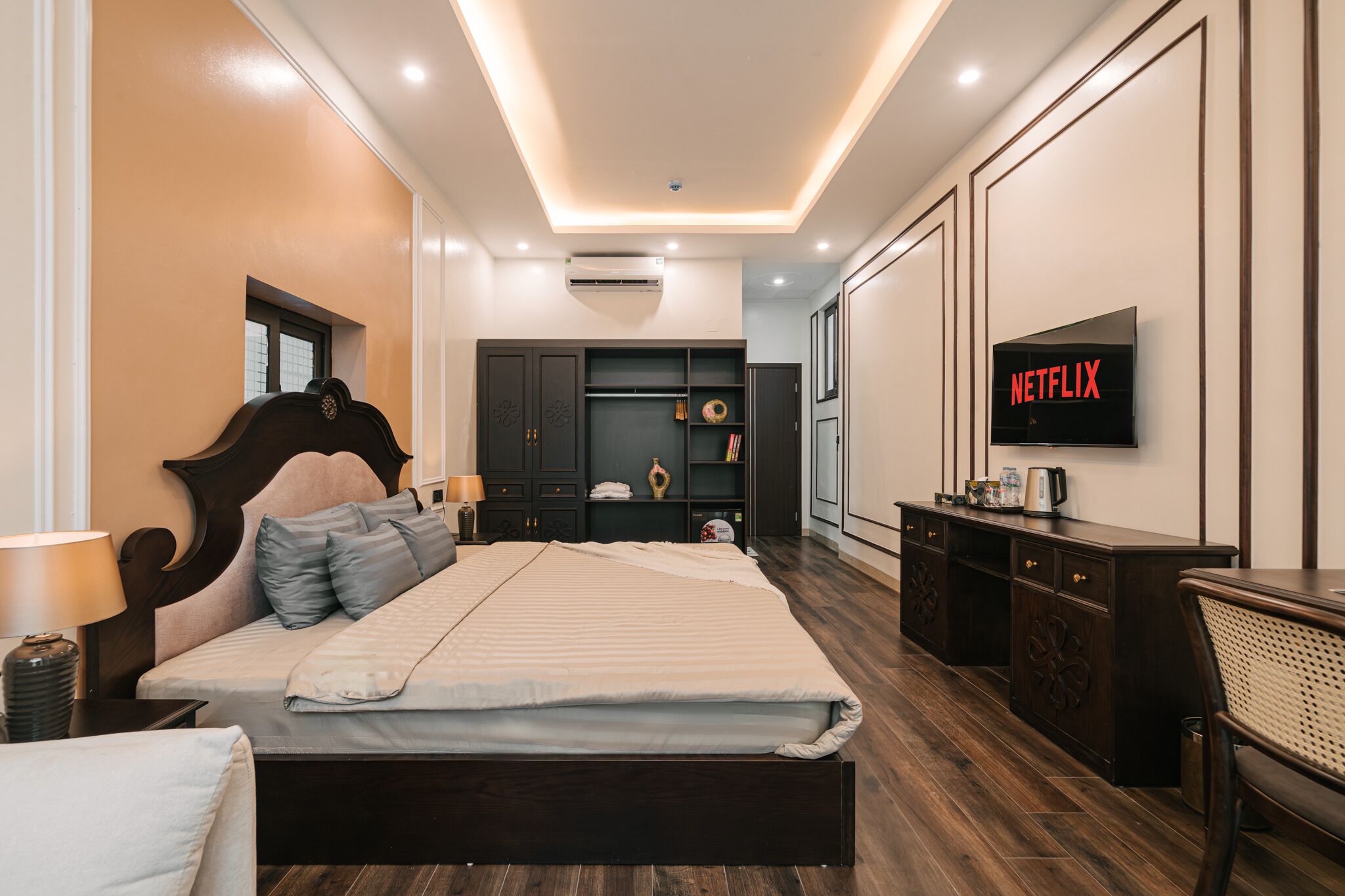 A modern bedroom with a bed, wardrobe, bedside table, lamp, and a TV displaying 'NETFLIX'.