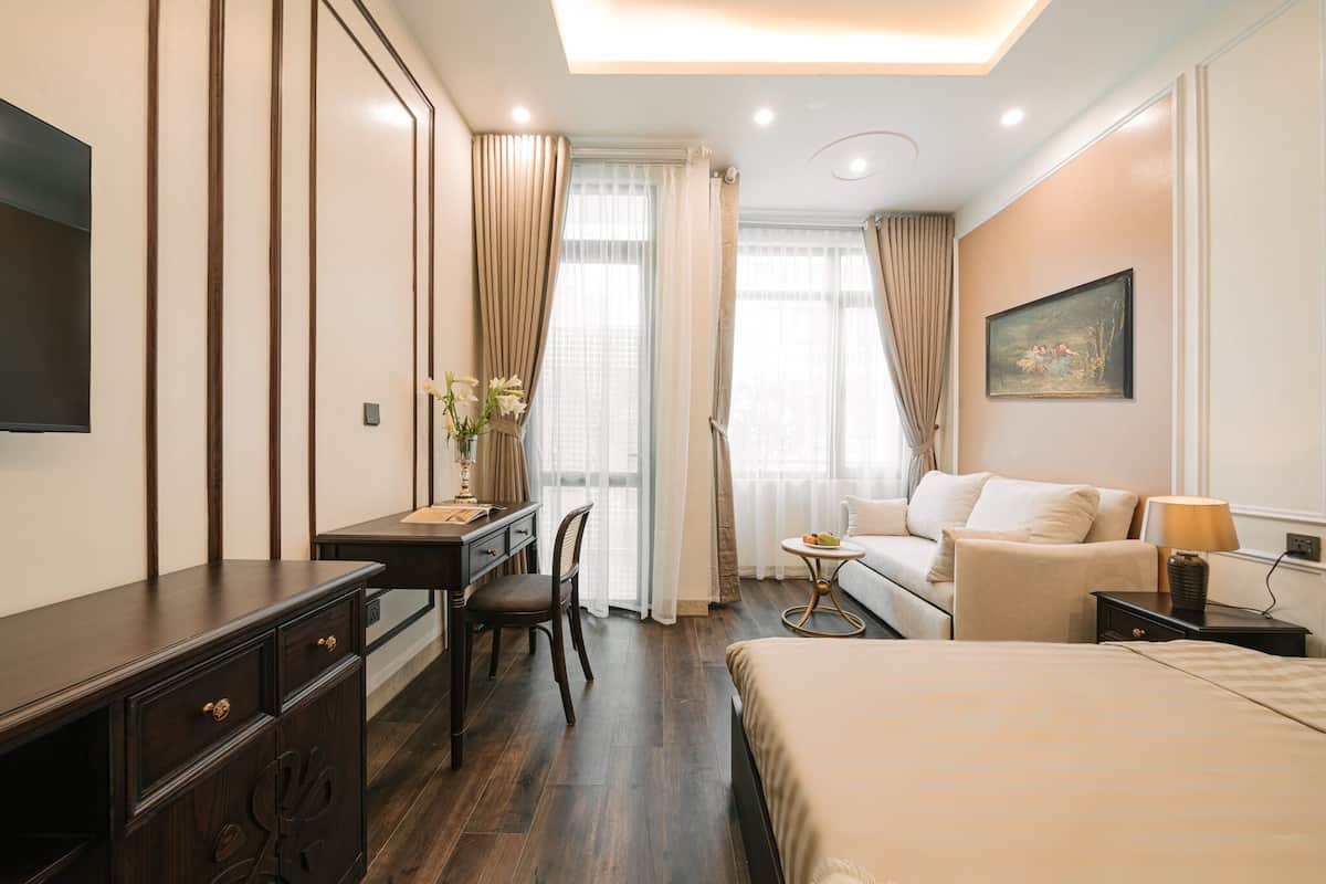 Ein Hotelzimmer mit einem Bett, einem Schreibtisch mit Stuhl, einer Couch, einem kleinen Tisch und einem an der Wand befestigten Fernseher.
