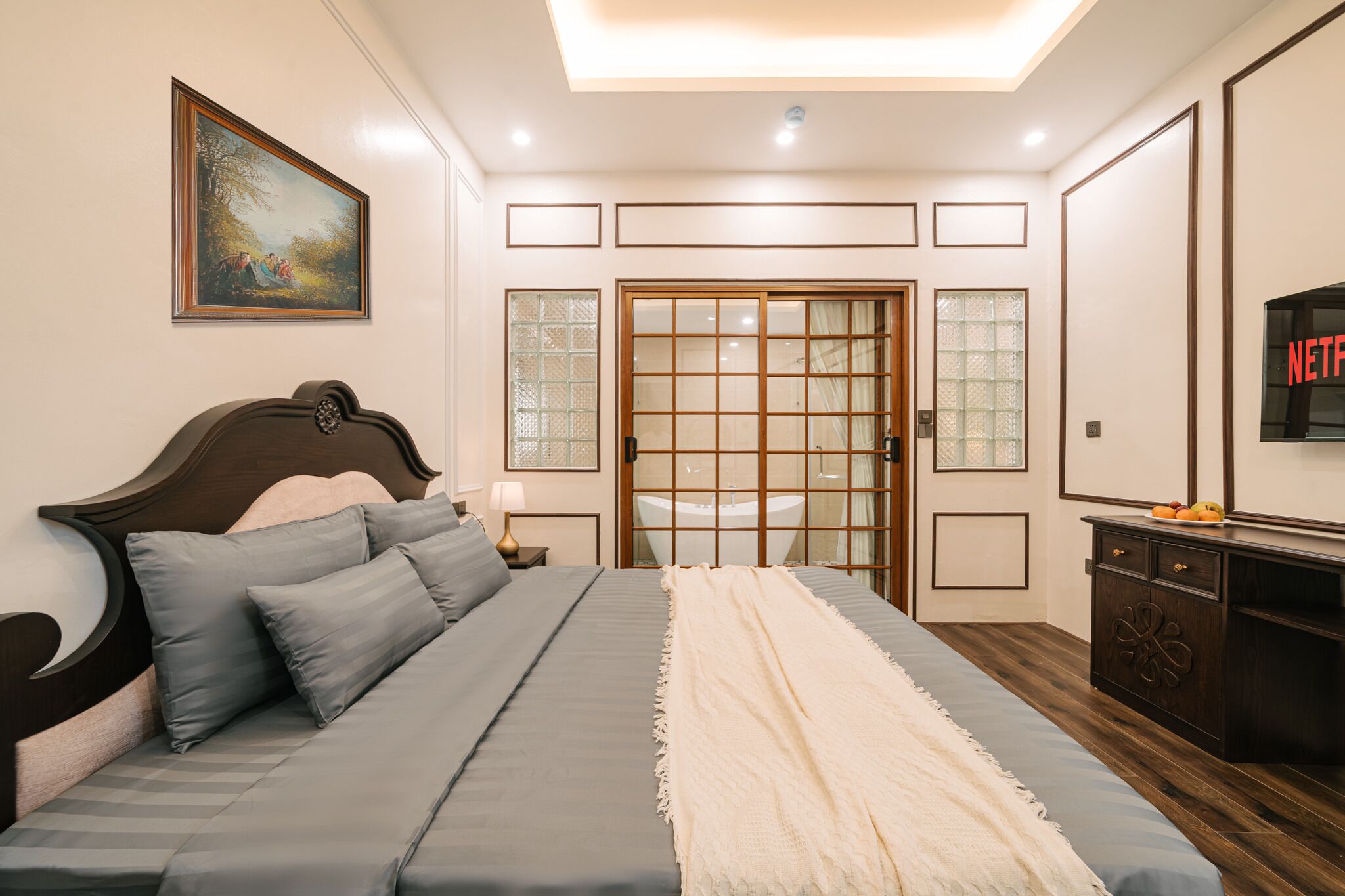 Un dormitorio con cama, cómoda, televisión y puerta con paneles de vidrio.