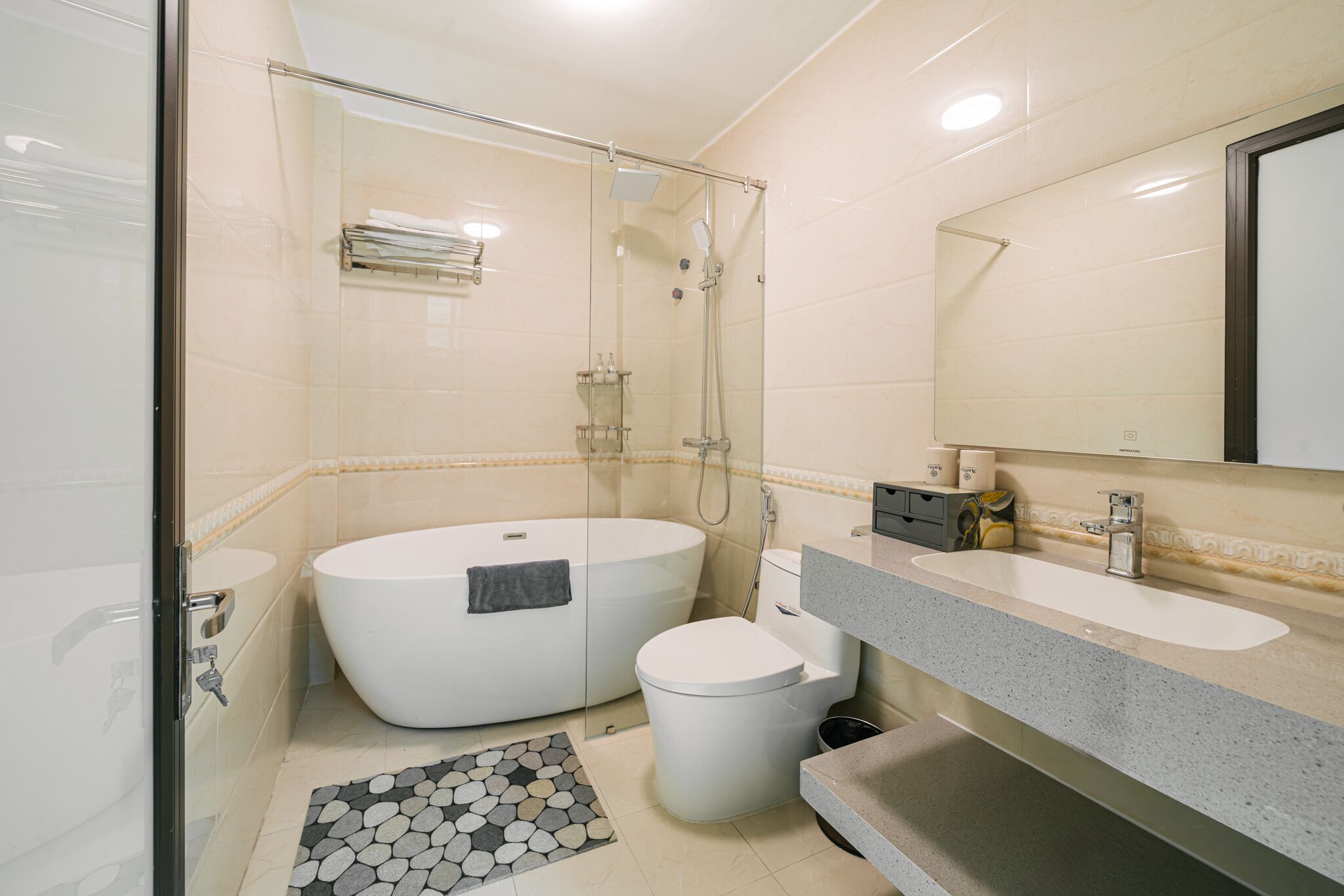 Ein modernes Badezimmer mit einer Glaskabine zur Dusche, einer freistehenden Badewanne, einer Toilette und einem Waschtisch mit Spiegel.