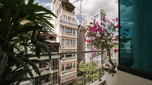 Un balcon donnant sur un immeuble à plusieurs étages, un pot de fleurs avec des fleurs roses et une enseigne avec du texte.