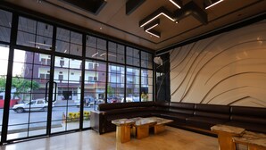 A modern lobby with large windows, a dark leather sofa, and a marble coffee table. - Hotel Guru Kripa Grand (3-Star Category)  (Mathura)